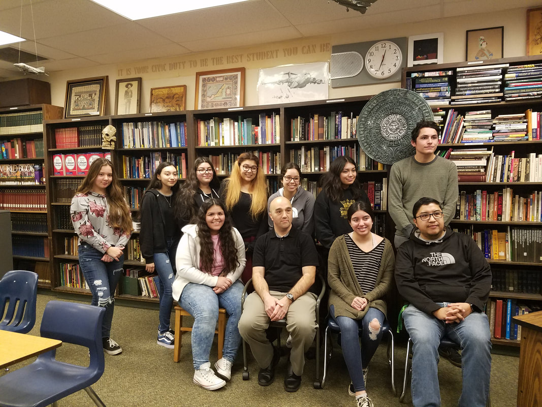 Picture of students standing in group with advisors in a room with bookshelves behind the students