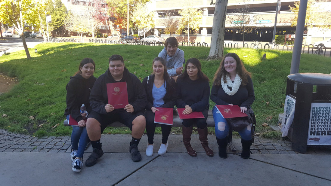 Picture students visiting the Chico State Campus, sitting on a bench with folders in their hands