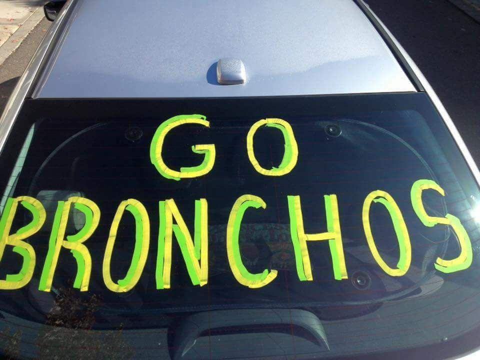 Photo of car windshield with GO BRONCHOS written on it in yellow & green