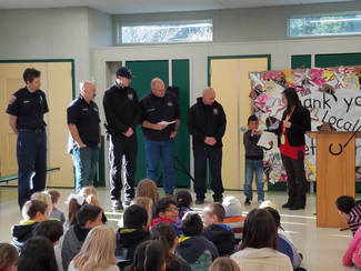 Picture of local fire fighters accepting thank you gifts from students gathered in the multi purpose room