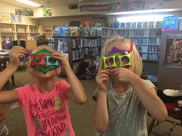 Picture of two students in the library with funny masks on